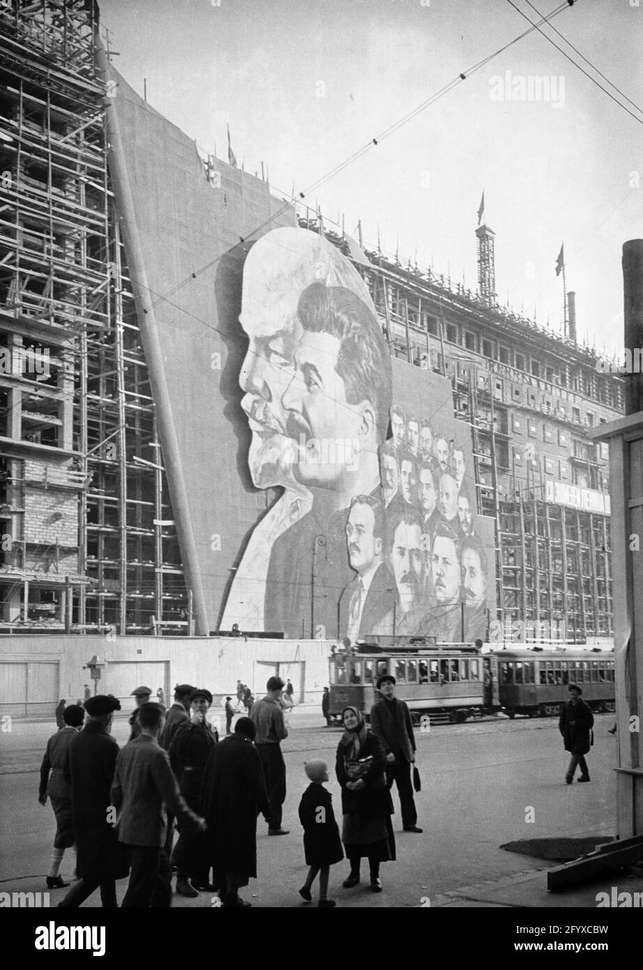Une grande affiche avec des portraits des dirigeants politiques russes Vladimir Lénine, Joseph Staline et d'autres pour le défilé du jour de mai pend sur l'échafaudage d'un bâtiment en construction, Moscou, Russie, 1934.(Photo de Burton Holmes) Banque D'Images