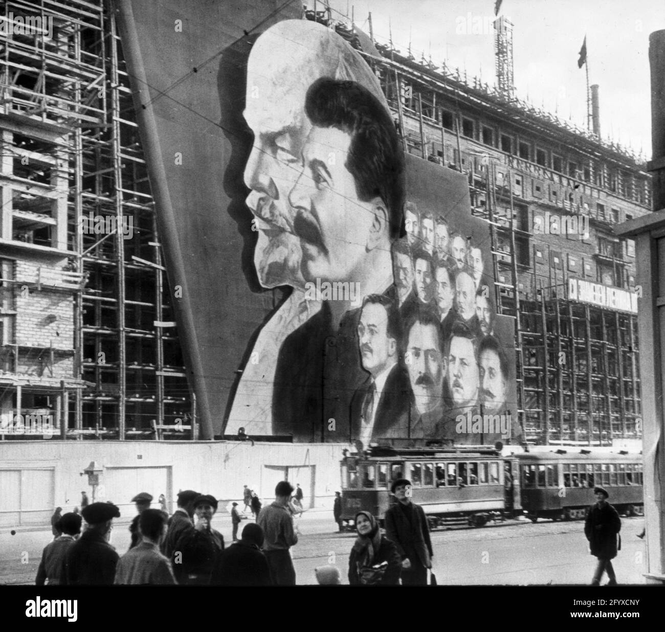 Une grande affiche avec des portraits des dirigeants politiques russes Vladimir Lénine, Joseph Staline et d'autres pour le défilé du jour de mai pend sur l'échafaudage d'un bâtiment en construction, Moscou, Russie, 1934.(Photo de Burton Holmes) Banque D'Images