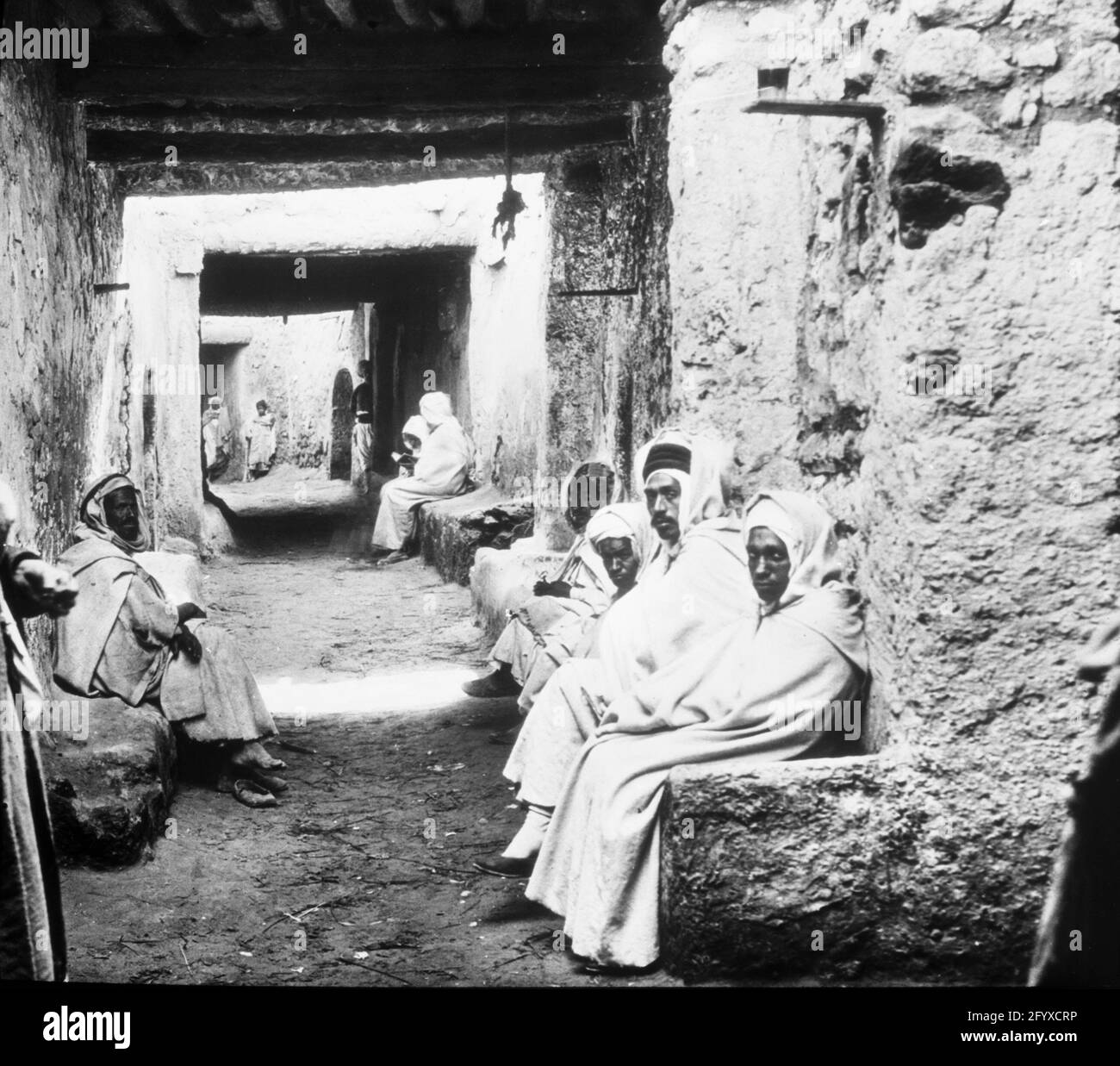 Des hommes vêtus de djellabas et de foulard de shesh sont assis dans une ruelle, Fès, Maroc, 1894. (Photo de Burton Holmes) Banque D'Images