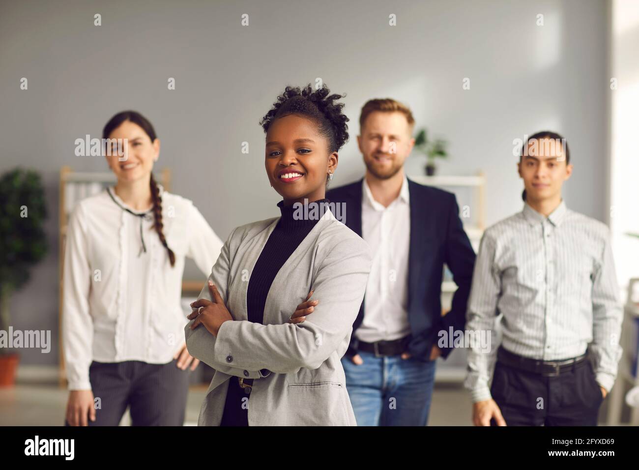 Femme d'affaires afro-américaine debout les bras repliés et souriant avec une équipe de les travailleurs derrière Banque D'Images