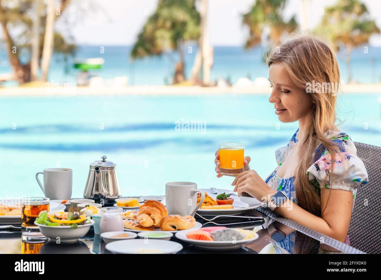 Femme souriante sur le petit déjeuner américain boire du jus d'orange à côté Piscine Banque D'Images