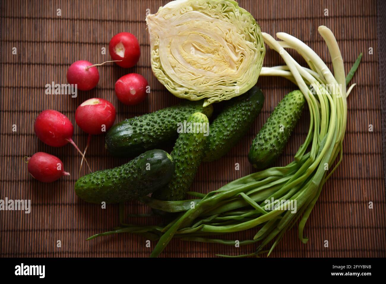 Légumes frais concombres, chou, oignons verts et radis se trouvent sur une serviette en bambou Banque D'Images