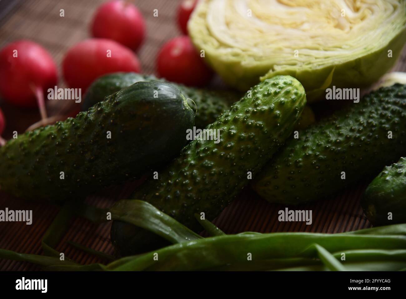 Légumes frais concombres, chou, oignons verts et radis se trouvent sur une serviette en bambou Banque D'Images