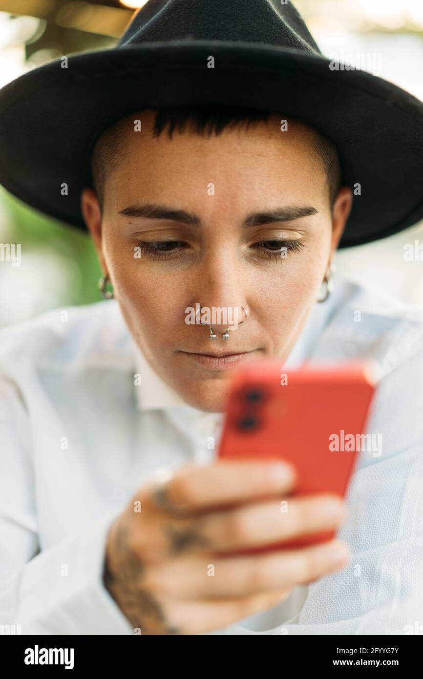 Femme masculine sérieuse portant une chemise blanche et un chapeau avec téléphone mobile assis dans un café Banque D'Images