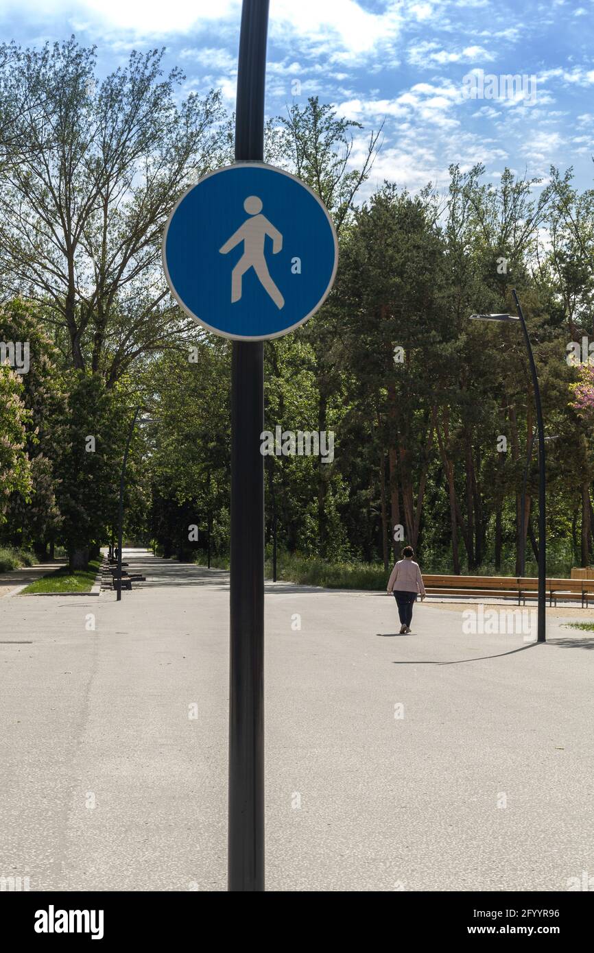 femme d'âge moyen marchant seule sur un large sentier avec un panneau bleu sur une journée ensoleillée entouré par le concept des arbres des soins de santé Banque D'Images