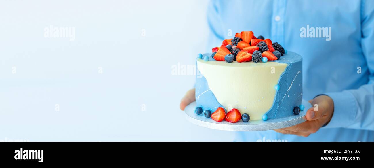 Une feuille de pâtisserie d'homme tenant un beau grand gâteau avec des baies dans ses mains. Cuisinier cuisinier cuisinier cuisinier ou boulanger masculin. Maquette copie concept de nourriture d'espace Banque D'Images