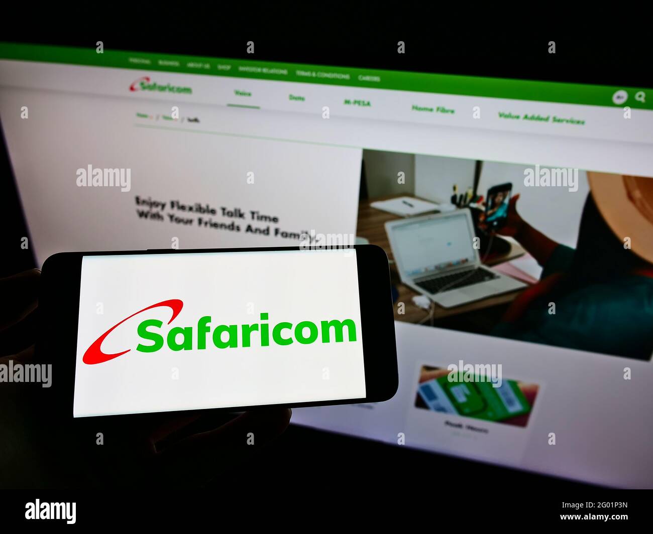 Personne tenant un téléphone portable avec le logo de la société kenyane de réseau mobile Safaricom PLC à l'écran en face de la page web. Mise au point sur l'affichage du téléphone. Banque D'Images