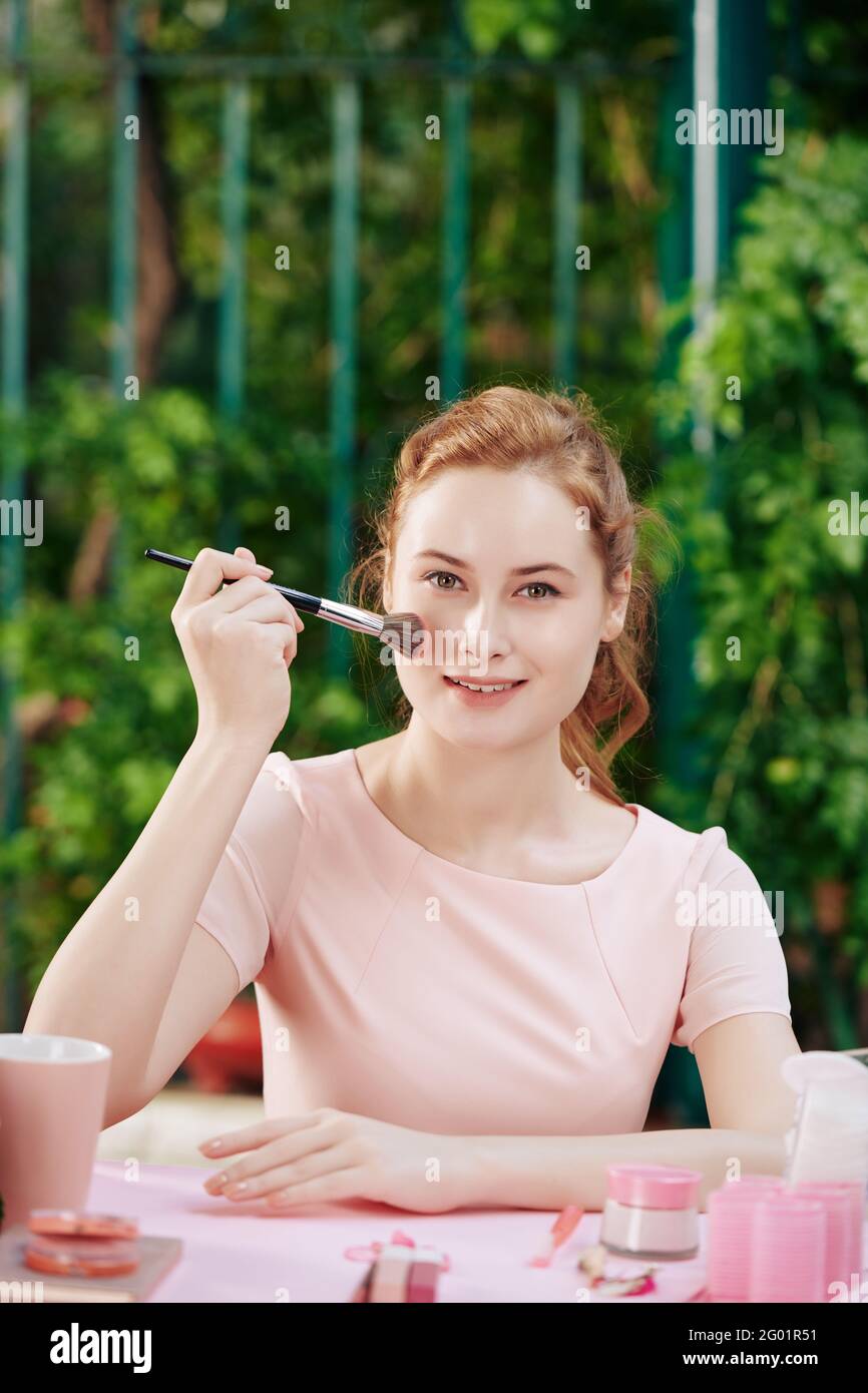 Jolie charmante jeune femme appliquant de la poudre pour le visage sur son nez avec une brosse synthétique moelleuse Banque D'Images