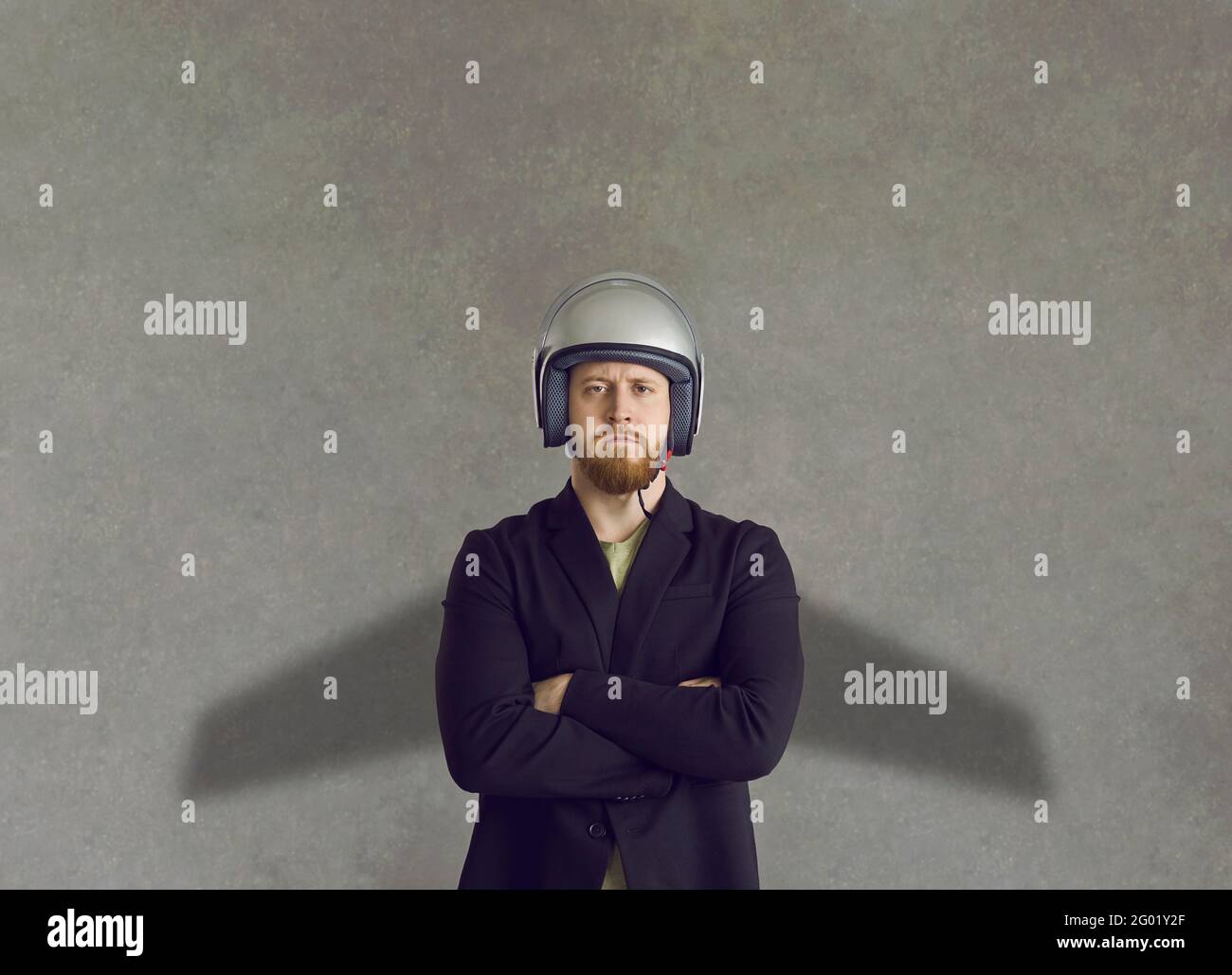 Homme d'affaires sérieux en casque debout et en jetant l'ombre du jet empaqueter les ailes sur le mur gris derrière Banque D'Images