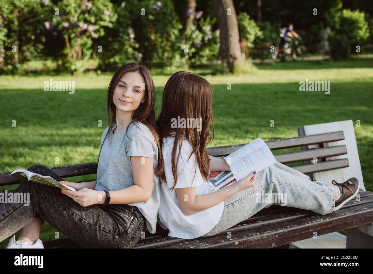 Deux étudiantes regardent un livre ouvert sur un banc dans le parc. Formation à distance, préparation aux examens. Mise au point sélective douce. Banque D'Images