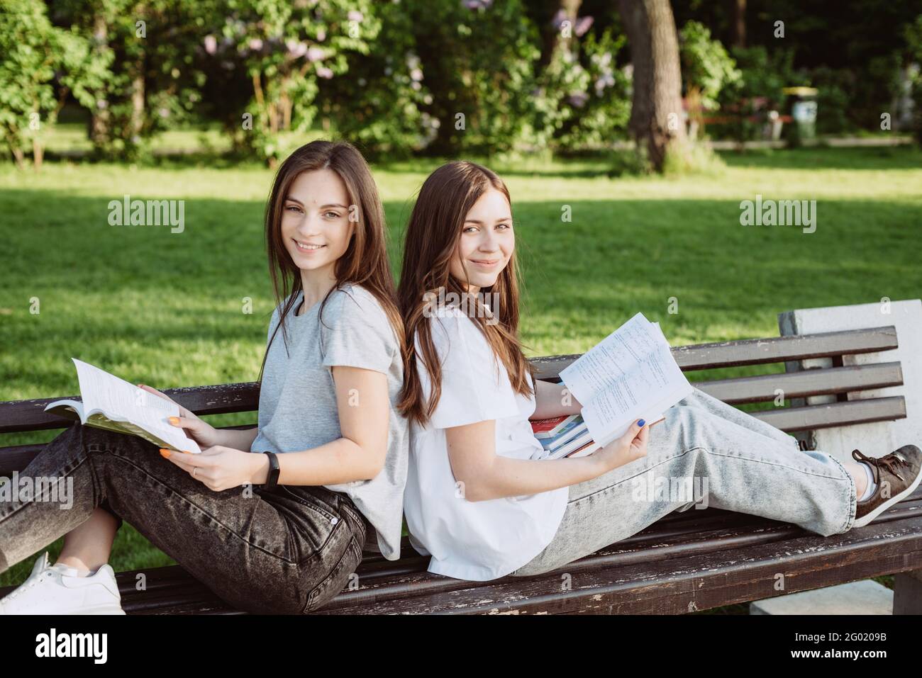 Deux étudiantes regardent un livre ouvert sur un banc dans le parc. Formation à distance, préparation aux examens. Mise au point sélective douce. Banque D'Images