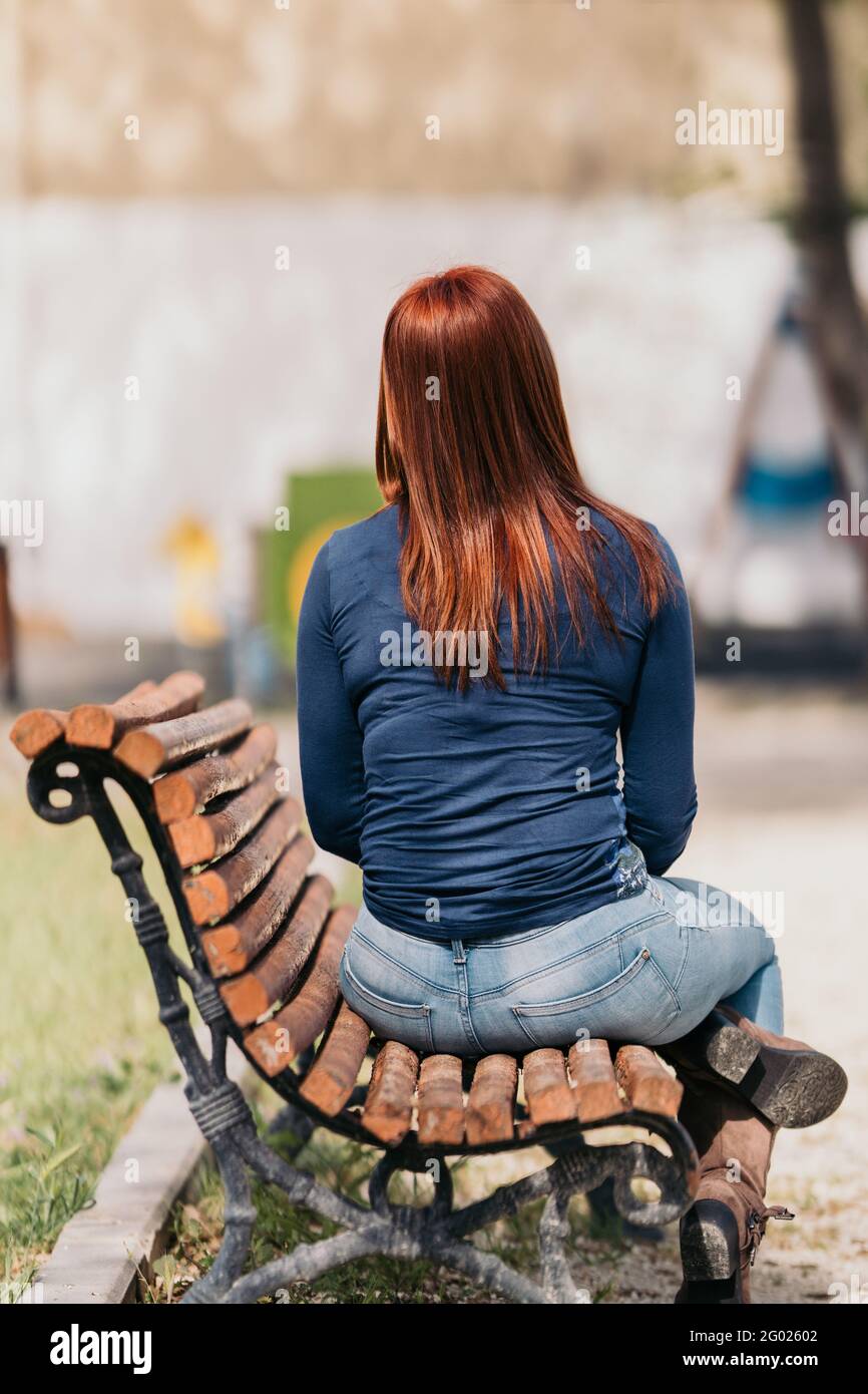 Une femme aux cheveux rouges assise sur un banc avec son dos à la caméra un jour ensoleillé. Tir américain. Banque D'Images