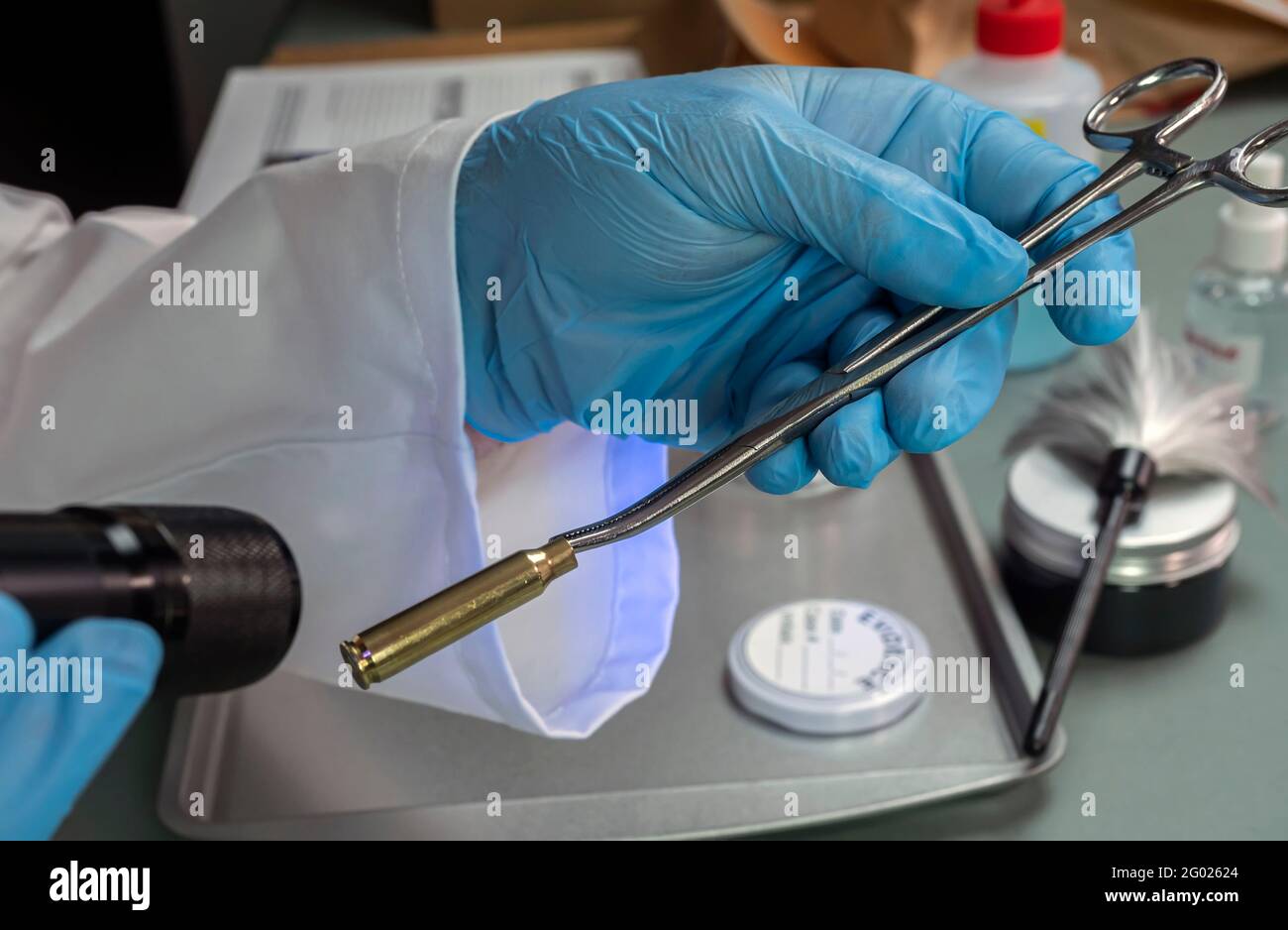 La police judiciaire examine le boîtier à balles avec une lampe UV pour rechercher les empreintes du suspect dans le meurtre, image conceptuelle Banque D'Images