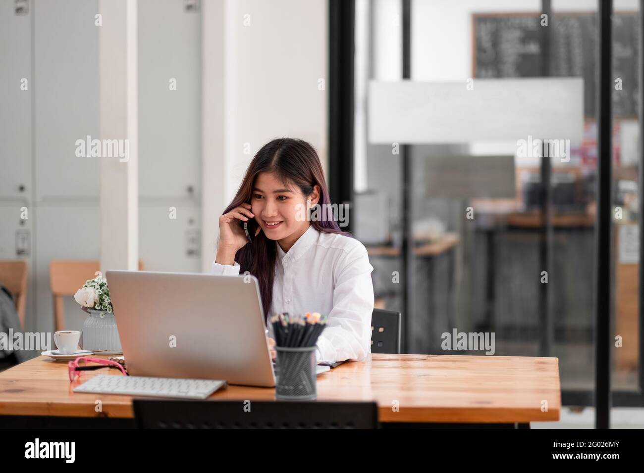 Photo de gaie positive asiatique jolie femme utilisant un ordinateur portable et parlant au téléphone. Banque D'Images