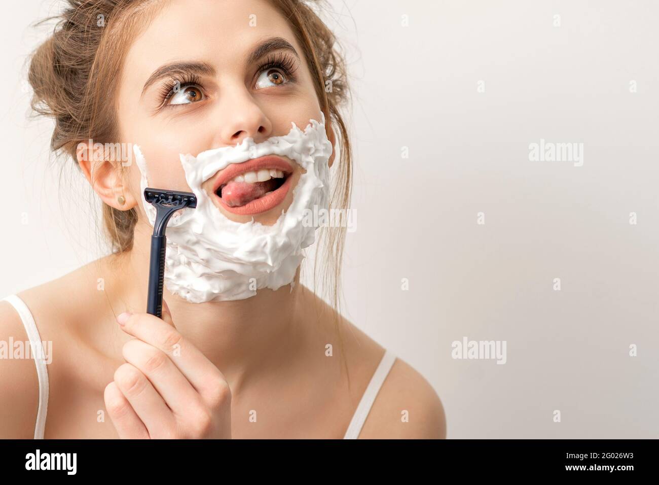 Belle jeune femme caucasienne souriante se raser le visage avec un rasoir  la langue doit être collée sur un fond blanc Photo Stock - Alamy