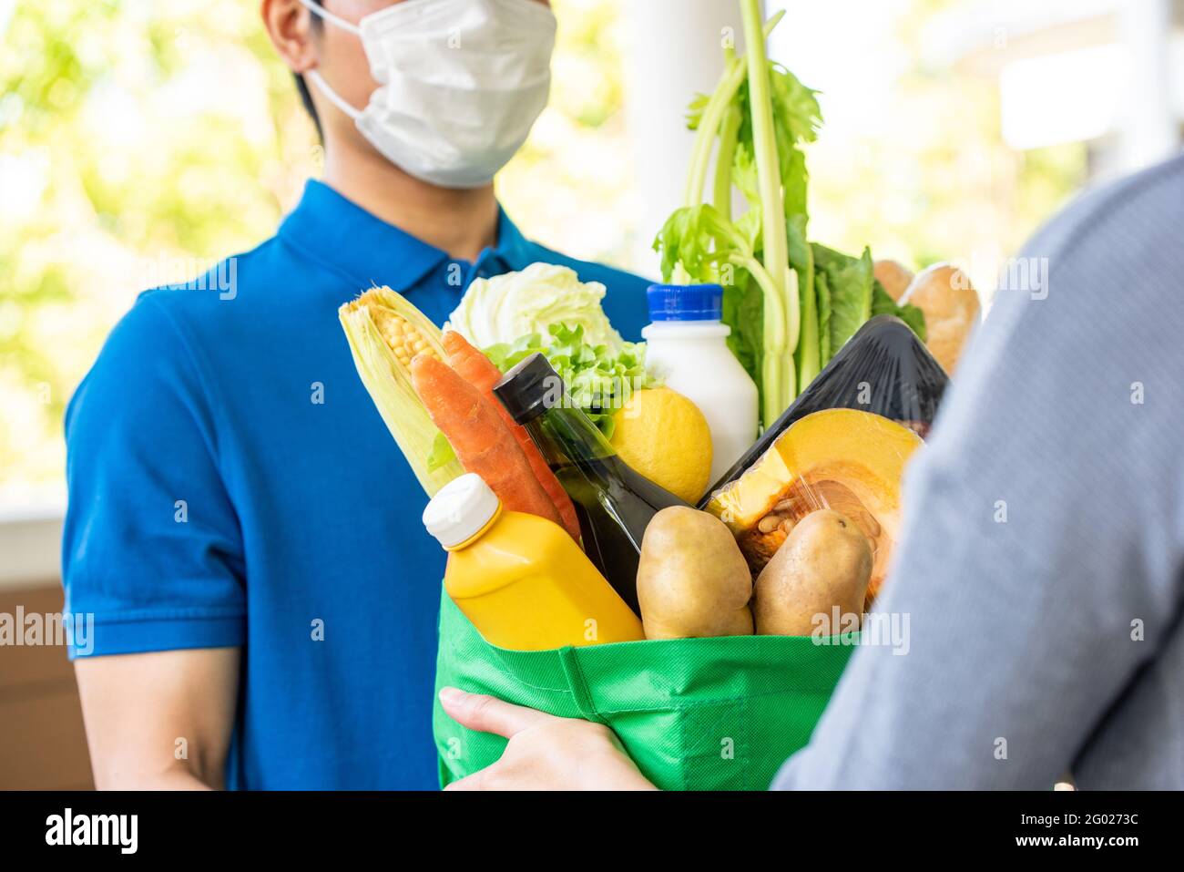 Homme de livraison asiatique en uniforme bleu portant un masque facial tout en livrant des produits alimentaires au client à la maison, livraison de nourriture en temps de pandémie concept Banque D'Images