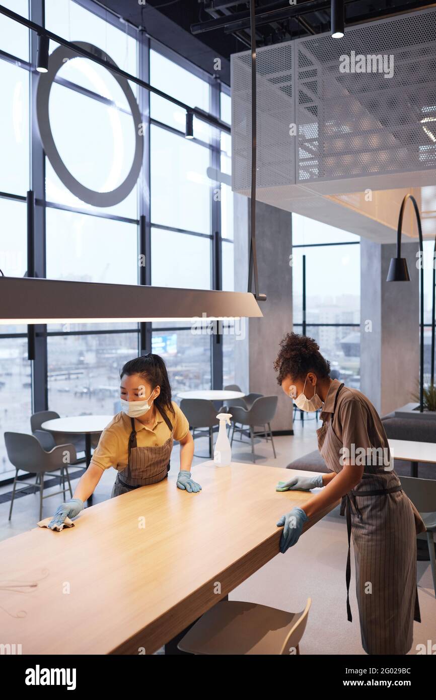 Portrait vertical de deux travailleuses portant des masques tout en nettoyant les tables dans l'intérieur moderne du restaurant, concept de sécurité covid, espace de copie Banque D'Images