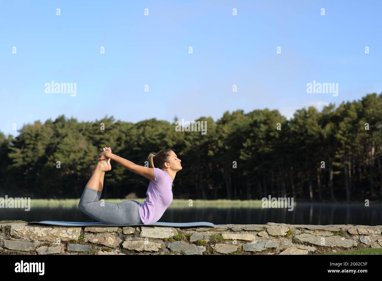 Profil d'une femme faisant le yoga pose dans la montagne à côté d'un lac Banque D'Images