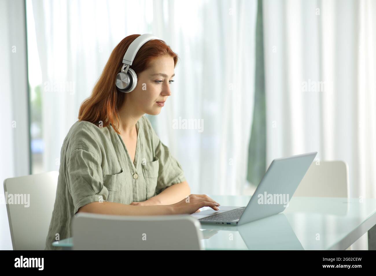 Femme concentrée avec casque sans fil vérifiant l'ordinateur portable à la maison Banque D'Images