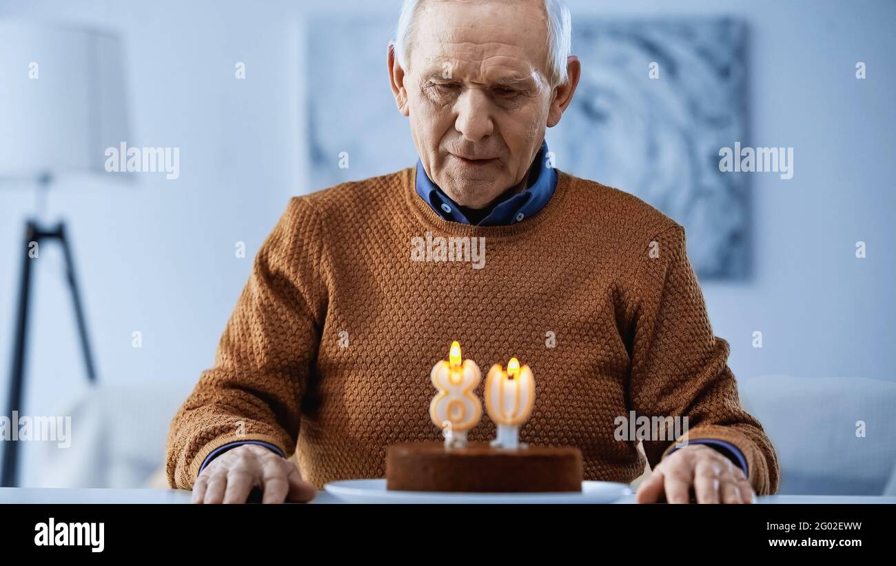 homme solitaire âgé regardant des bougies allumées sur le gâteau d'anniversaire dans la salle de séjour Banque D'Images