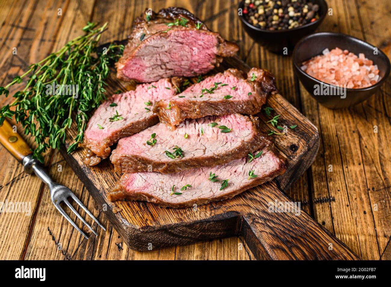 Tranches rares de rôti de boeuf sirloin à trois pointes steak bbq sur une planche à découper en bois. fond en bois. Vue de dessus Banque D'Images