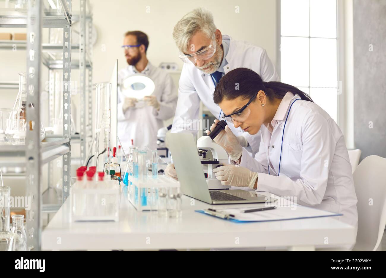 Scientifique effectuant l'expérience en utilisant le microscope sous contrôle superviseur Banque D'Images