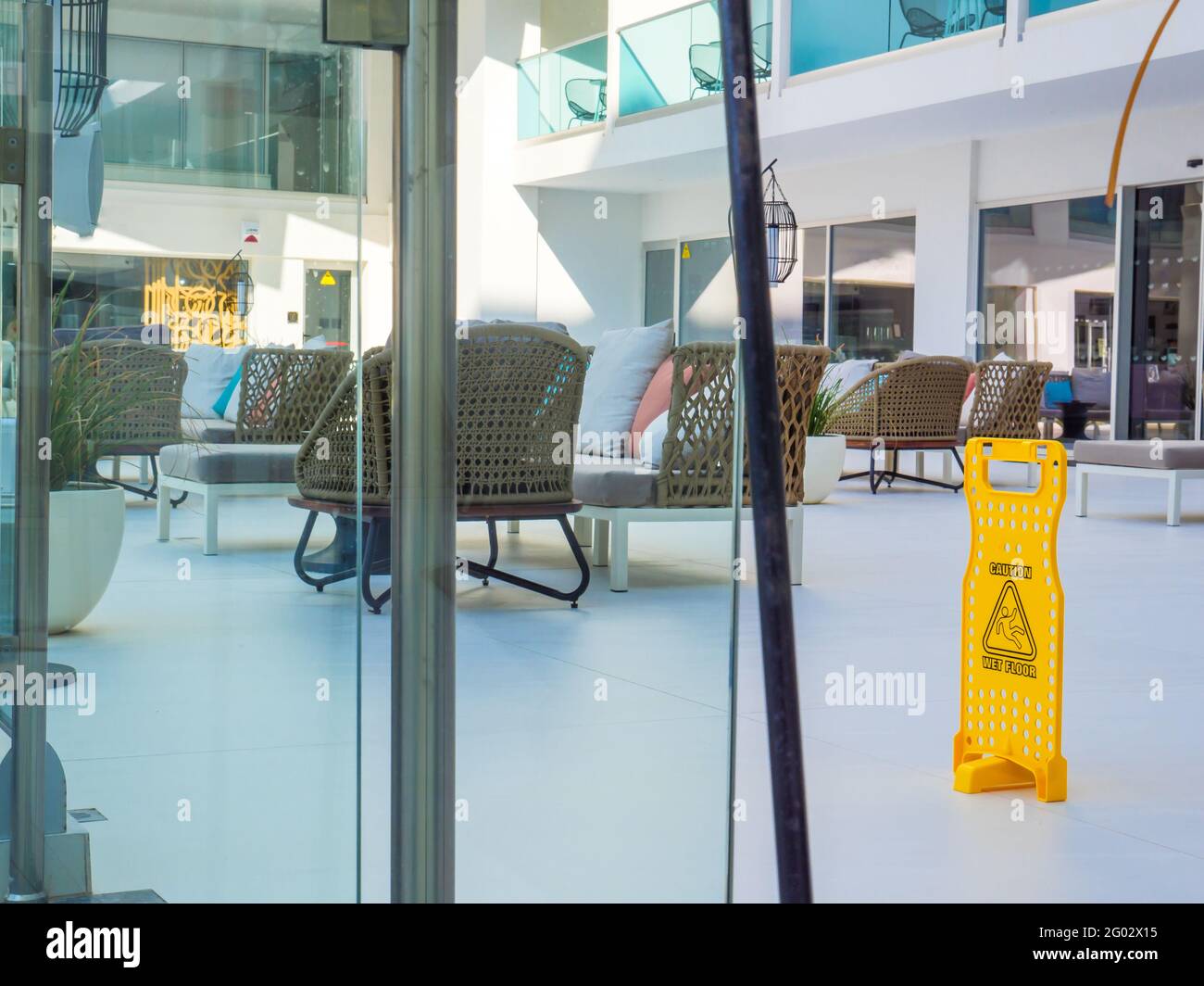 Panneau d'avertissement en plastique jaune sol humide sur la terrasse d'un hôtel à Napa, Chypre. Fauteuils et canapés de cricket vides avec coussins en arrière-plan. Banque D'Images