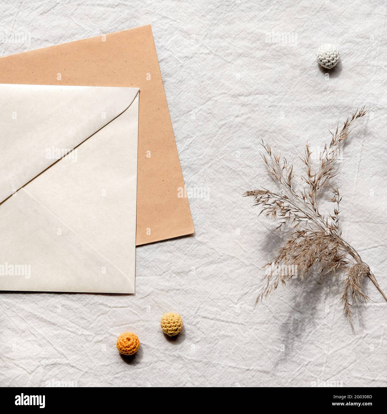 Plat en tissu carré avec carte, enveloppe, roseaux secs, pampas d'herbe. Fond de nappe en coton blanc cassé avec boules de coton tricotées. Simple minimale Banque D'Images
