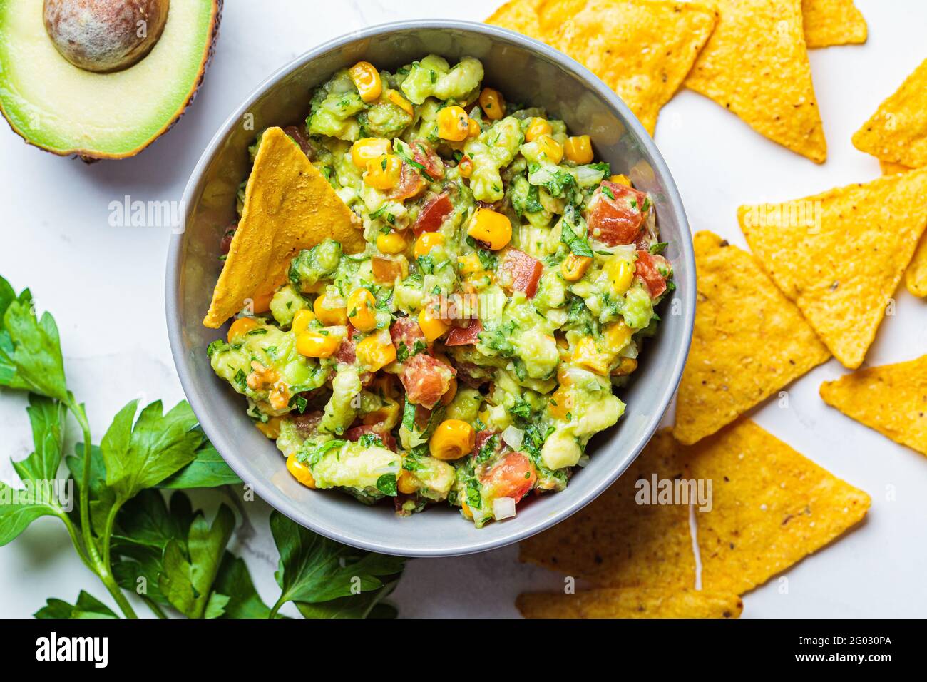 Trempez le guacamole à l'avocat avec du maïs grillé dans un bol gris. Concept alimentaire végétalien, cuisine mexicaine. Banque D'Images