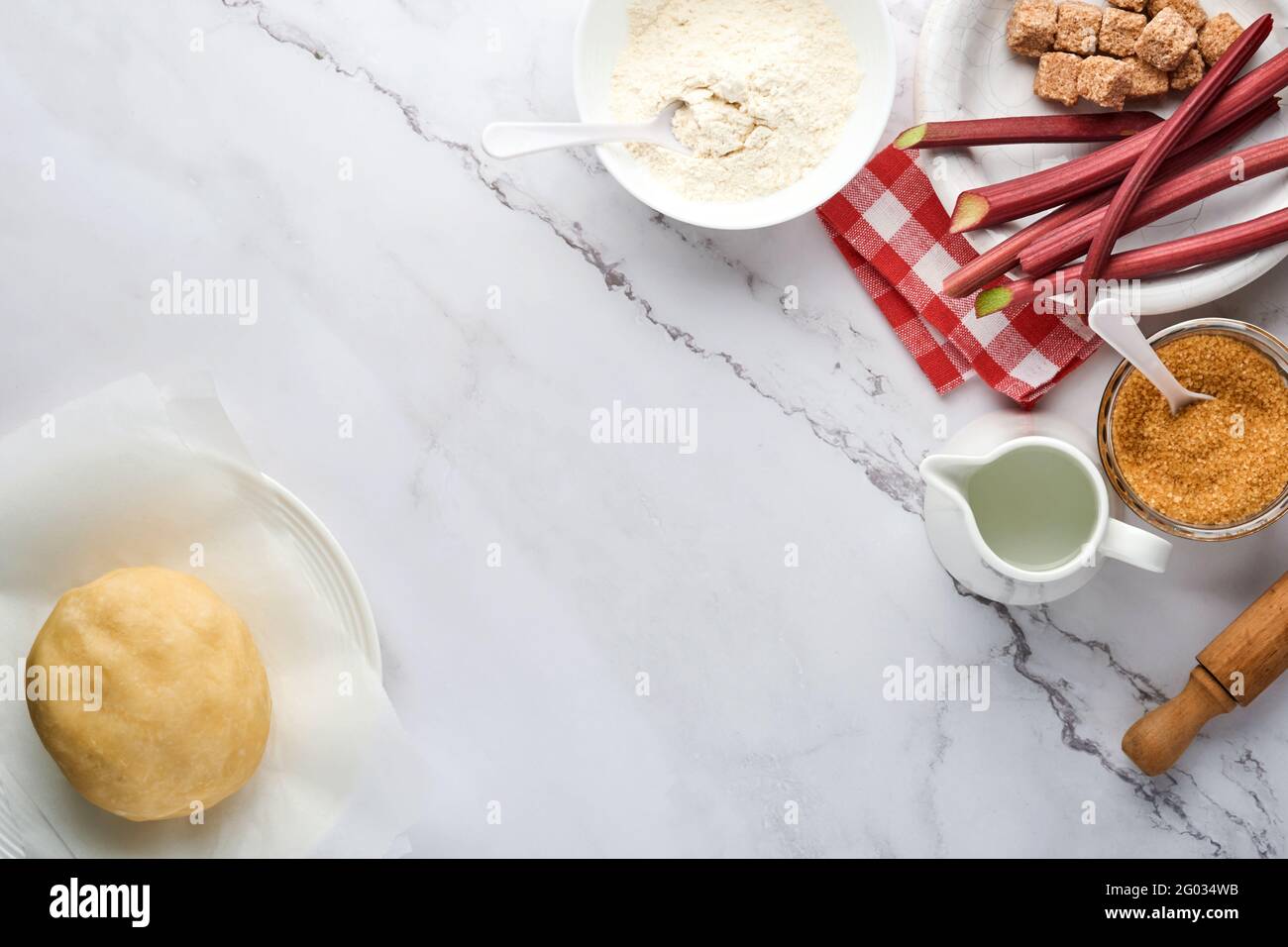 Boule de pâte et ingrédients farine, eau, beurre, sucre et rhubarbe pour cuire sur fond de marbre blanc avec dépoussiérage de farine. Recette étape par étape Banque D'Images