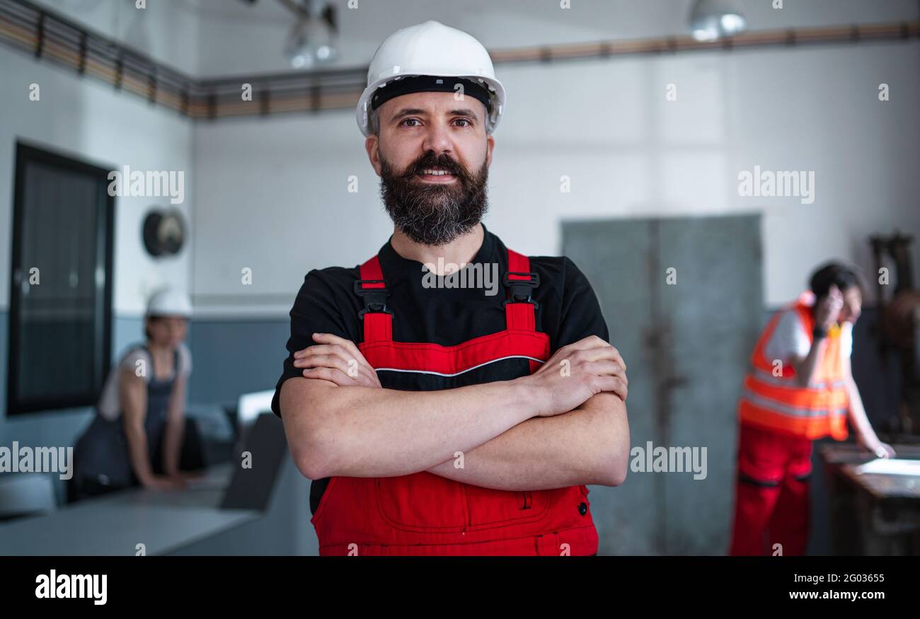 Portrait d'un travailleur avec un casque à l'intérieur en usine regardant la caméra. Banque D'Images