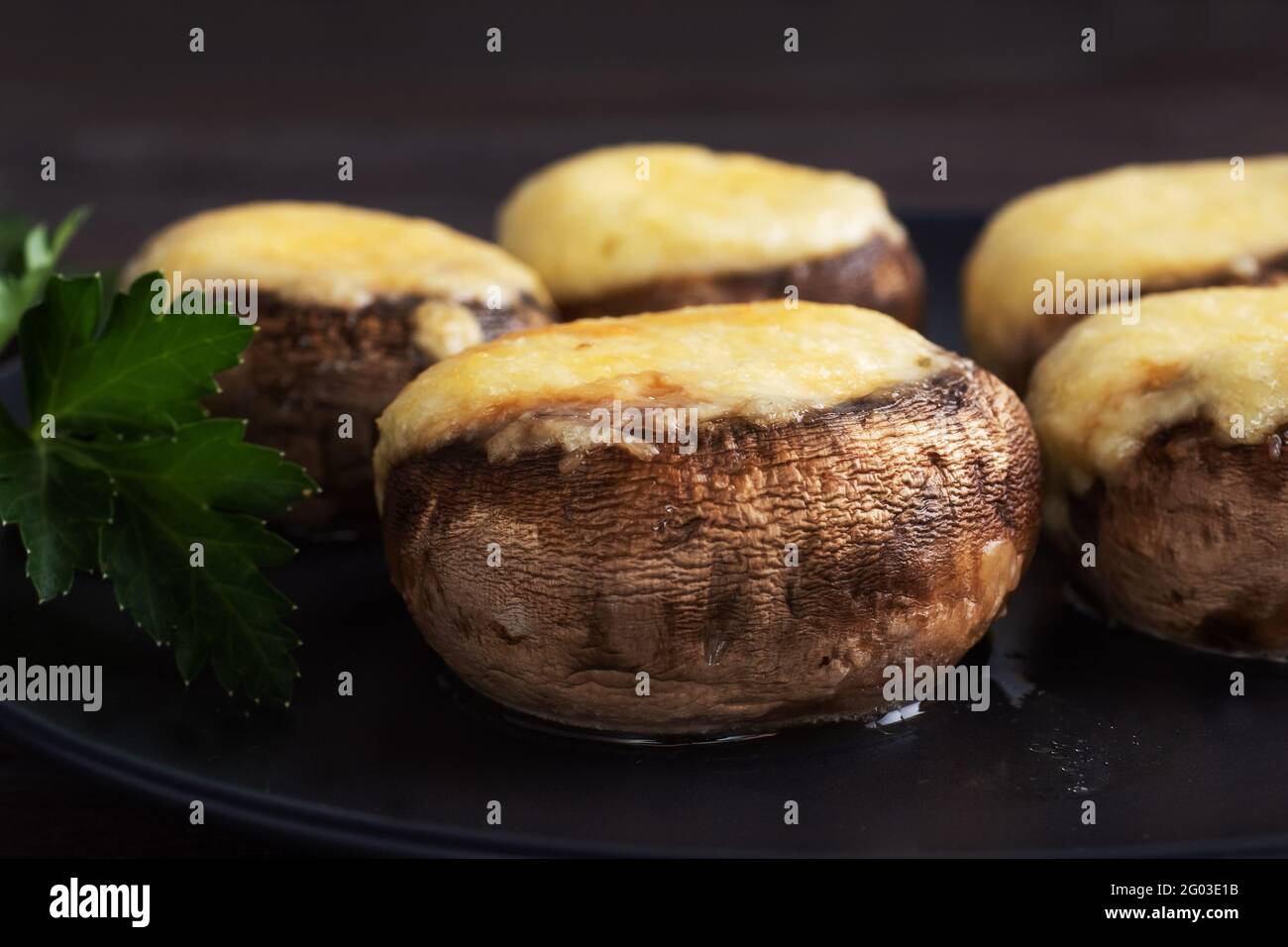 Champignons cuits farcis au fromage et aux herbes sur une assiette noire. fond en bois Banque D'Images Champignons cuits farcis au fromage et aux herbes sur une assiette noire. fond en bois Banque D'Images
