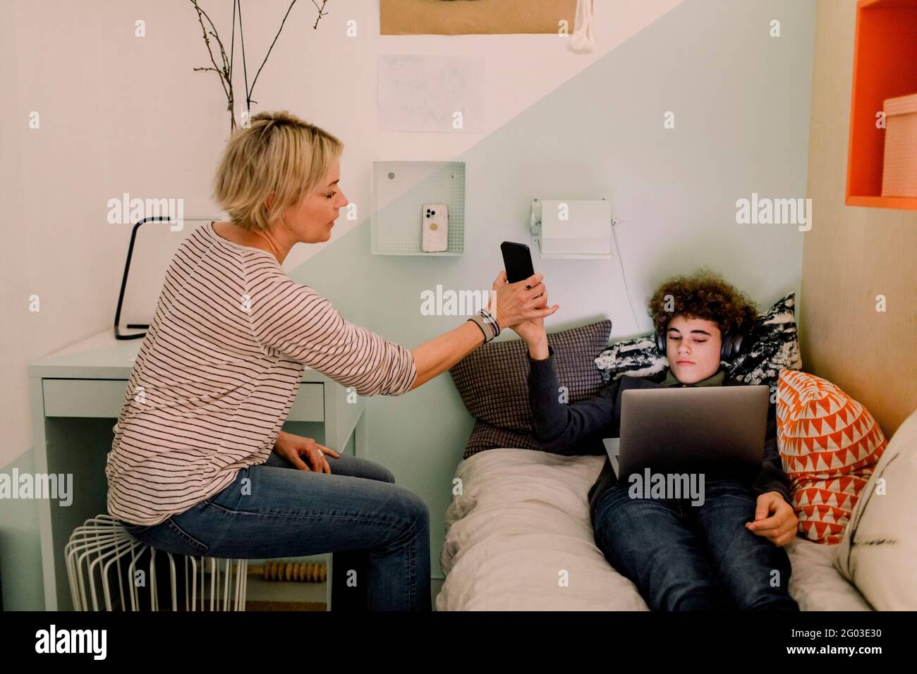 Garçon donnant un smartphone à la mère tout en étant allongé avec un ordinateur portable sur le lit à la maison Banque D'Images