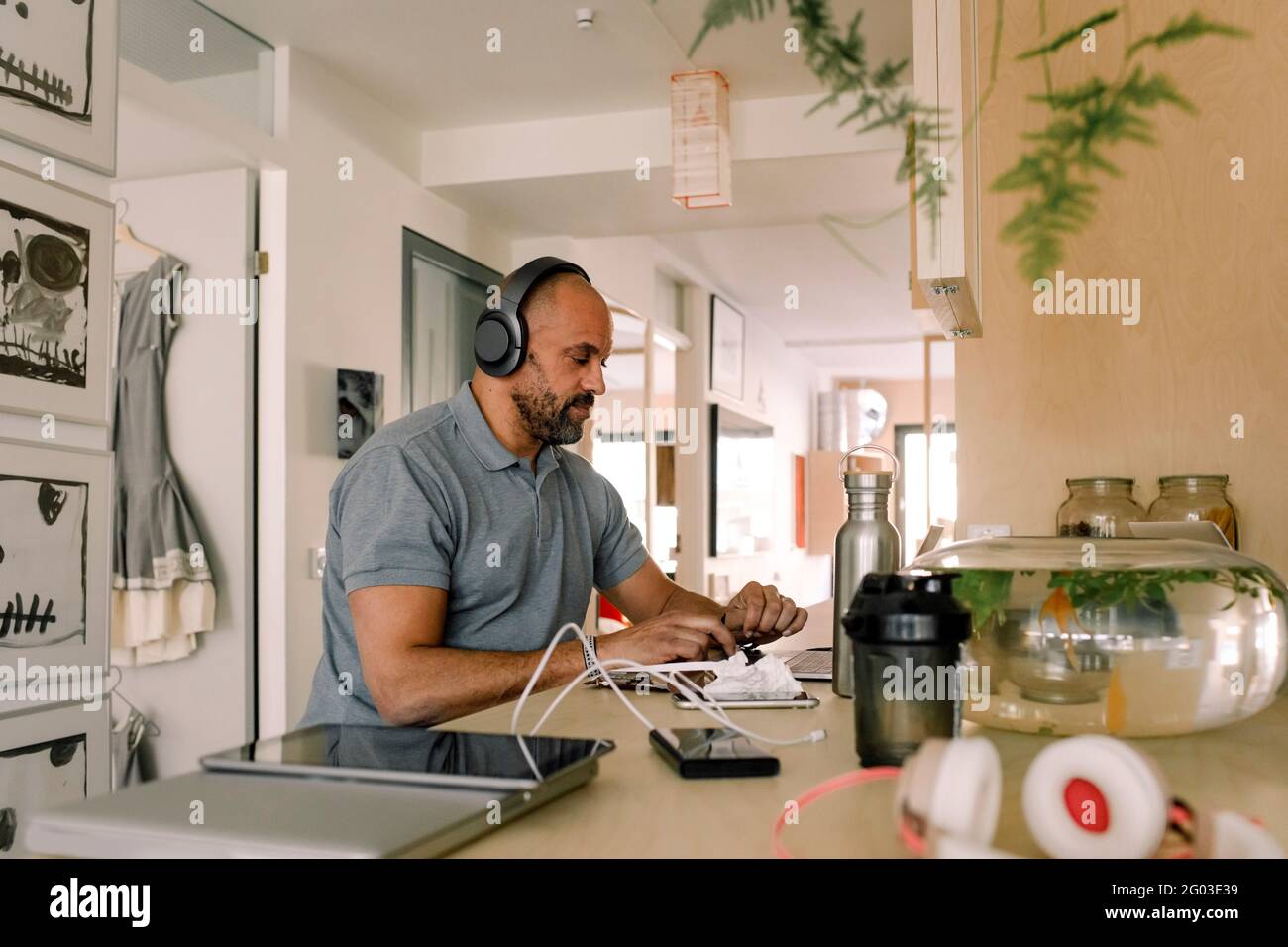 Homme d'affaires portant des écouteurs travaillant sur un ordinateur portable tout en étant assis dans un îlot de cuisine Banque D'Images