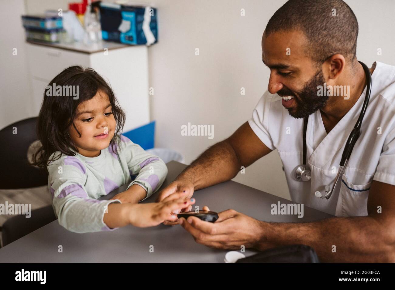 Homme souriant pédiatre vérifiant le niveau de sucre de la fille dans la clinique médicale Banque D'Images