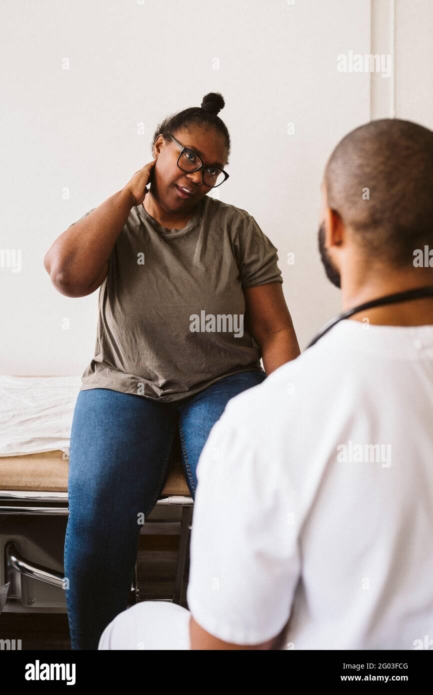 Femme adulte de taille moyenne consultant un médecin de sexe masculin au sujet de douleurs au cou à la clinique médicale Banque D'Images