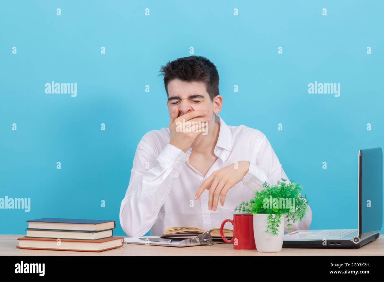 un étudiant lassé ou fatigué qui baille à la réception avec des livres et l'ordinateur Banque D'Images