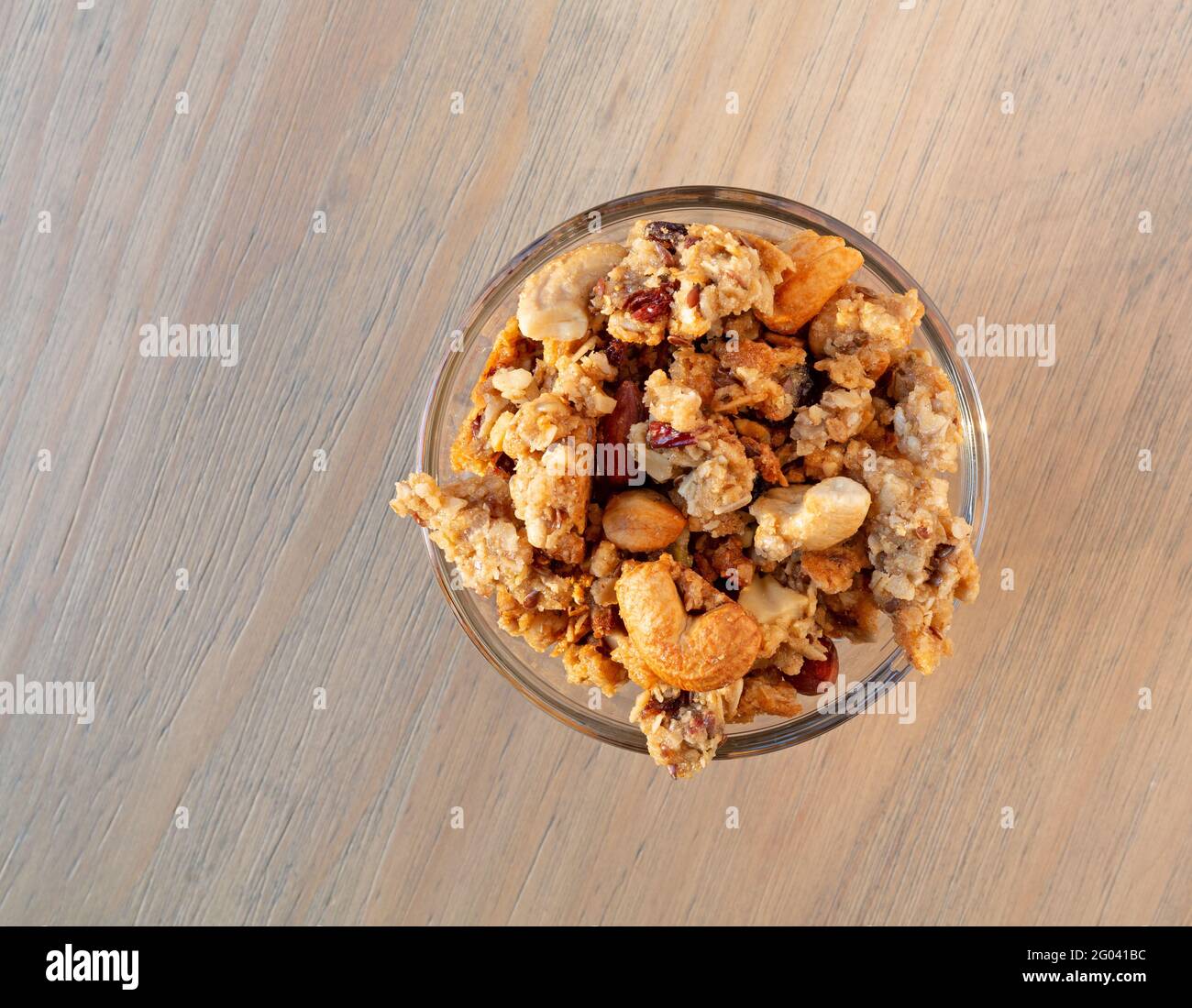 Vue de dessus d'un petit bol en verre rempli de céréales complètes granola avec fruits et noix sur une table. Banque D'Images