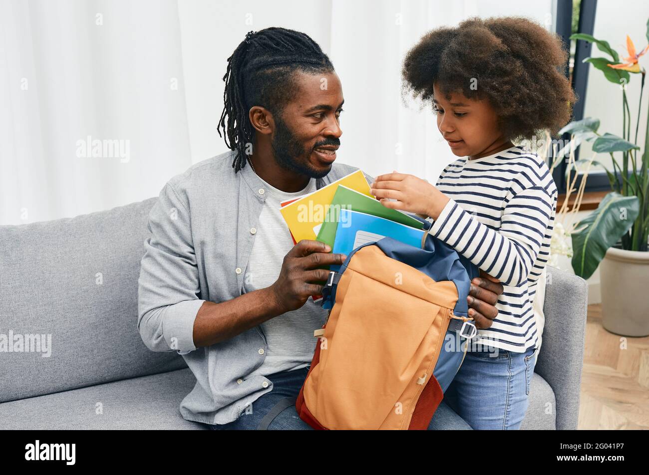 Le père aide la fille à mettre des copybooks de couleur dans le sac d'école avant une journée d'école Banque D'Images