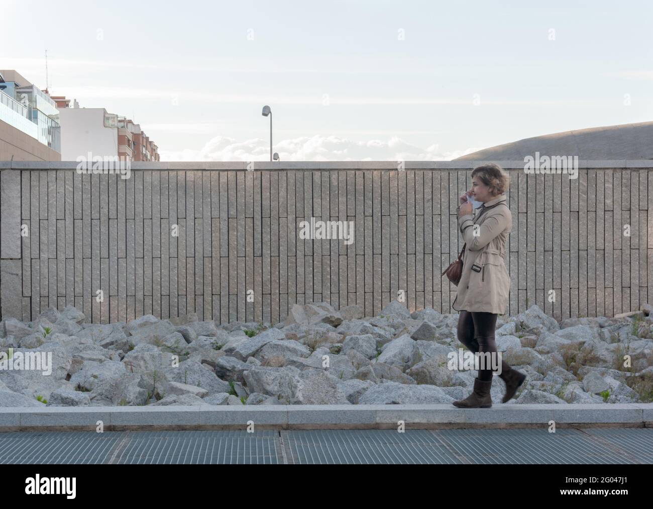 Jolie et élégante femme d'âge moyen qui prend son visage masque de marche dans la ville avec un mur de briques et des pierres en arrière-plan Banque D'Images