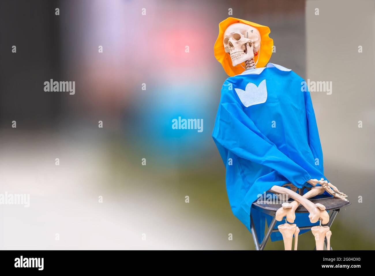 Squelette anatomique humain flexible souriant pour l'enseignement de l'anatomie médicale assis sur une chaise pliante et portant un chapeau jaune et des vêtements bleus contre un blu Banque D'Images