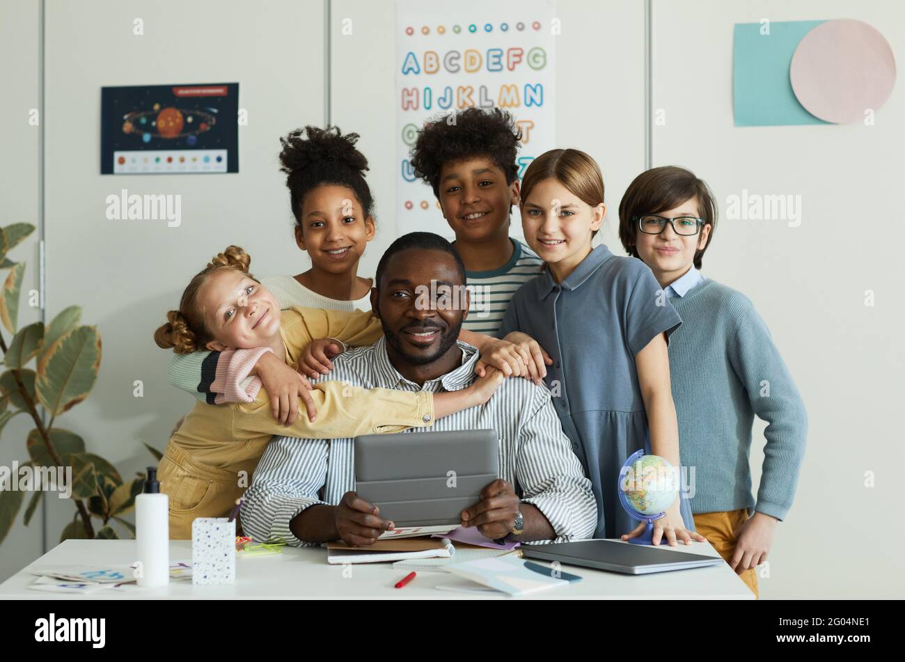 Portrait d'un groupe diversifié d'enfants à la recherche d'un enseignant masculin à la caméra dans la salle de classe Banque D'Images