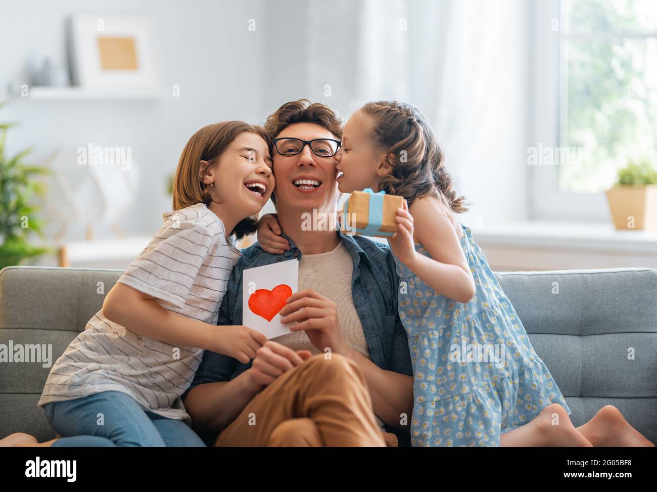 Les enfants filles félicitaient leur père et lui donnent une carte postale. Papa et les filles sont souriantes et embrassantes. Vacances en famille et ensemble. Banque D'Images