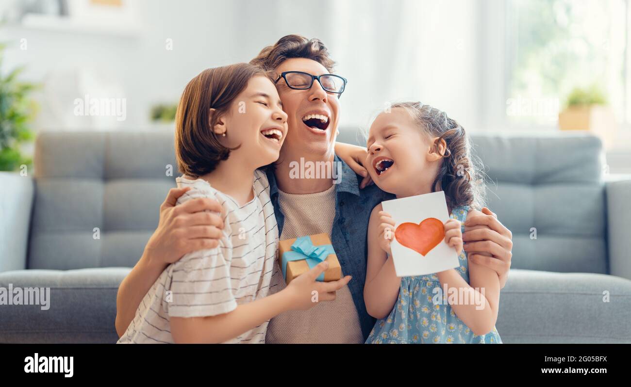Les enfants filles félicitaient leur père et lui donnent une carte postale. Papa et les filles sont souriantes et embrassantes. Vacances en famille et ensemble. Banque D'Images