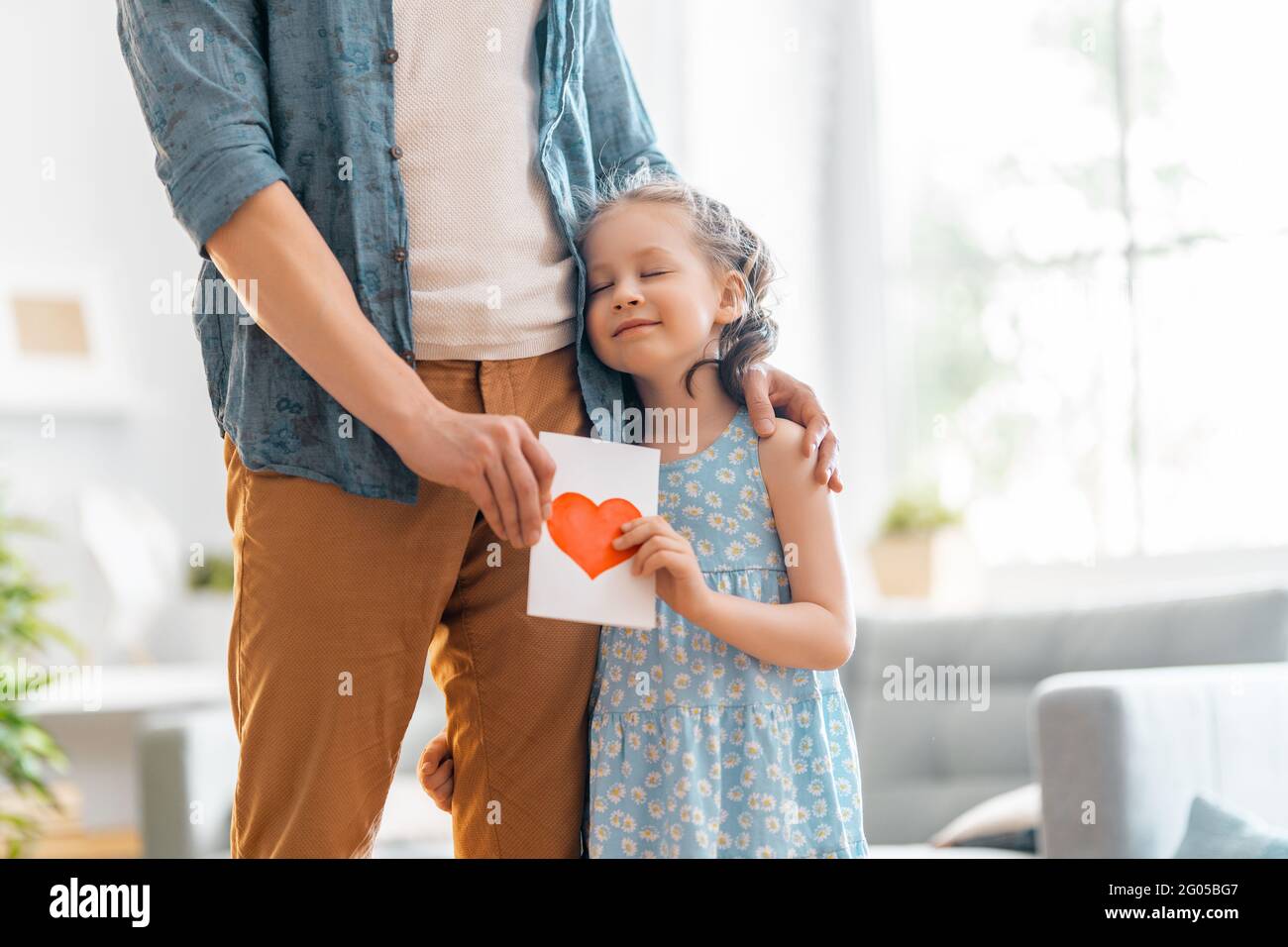 L'enfant fille félicite son père et lui donne une carte postale. Papa et fille sont souriants et embrassant. Vacances en famille et ensemble. Banque D'Images