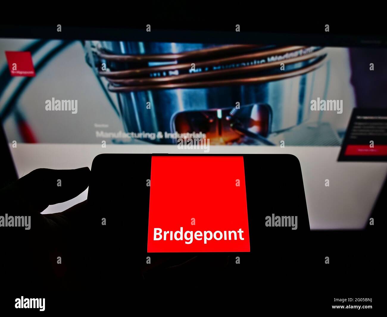 Personne tenant un téléphone portable avec le logo de la société privée Bridgepoint Advisers Limited à l'écran en face de la page Web. Mise au point sur l'affichage du téléphone. Banque D'Images