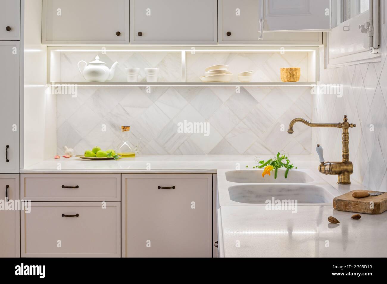 Cuisine élégante avec accessoires. Intérieur beige clair avec étagères éclairées et légumes frais sur table. Décoration de style vintage. Banque D'Images