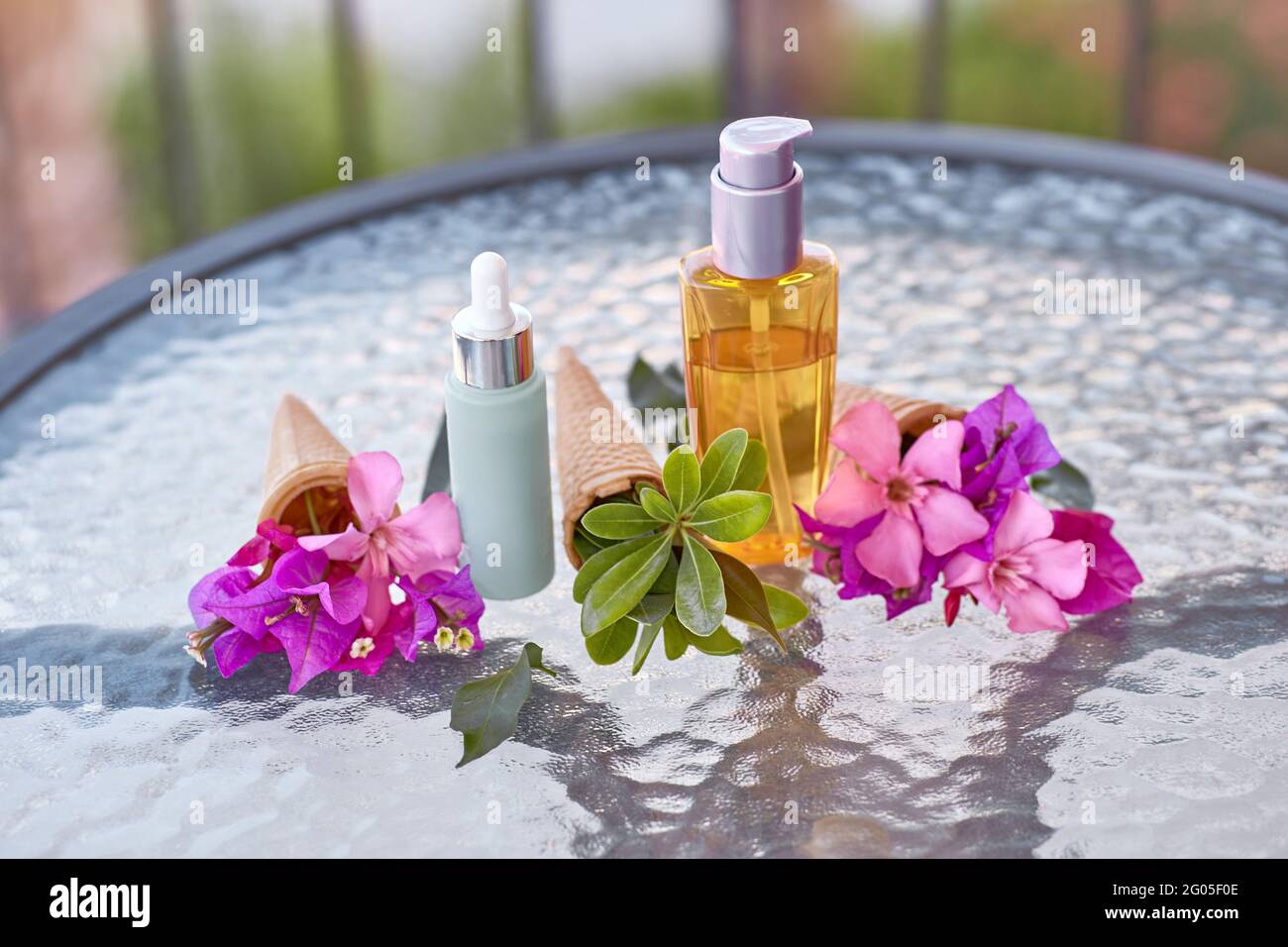 Bougainvilliers rose vif surréaliste fleurit dans un cône de crème glacée et maquette de bouteilles cosmétiques. Bouteille de maquillage d'huile et bouteille de verre à gouttelettes. Produits de beauté d'été Banque D'Images