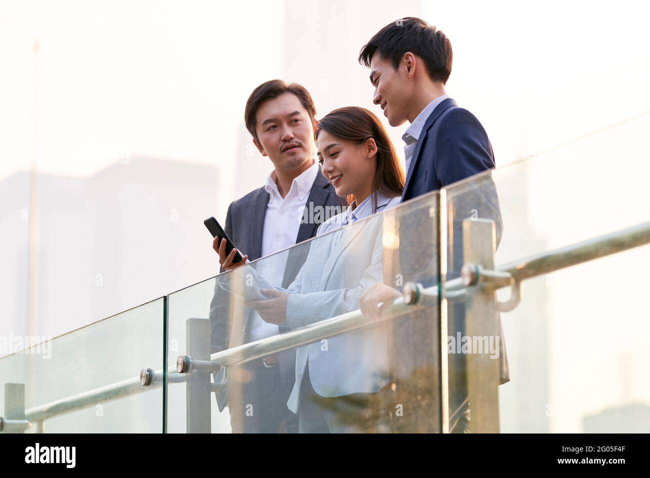trois heureux hommes d'affaires asiatiques regardant le téléphone portable bavardant discuter pour les affaires en extérieur Banque D'Images