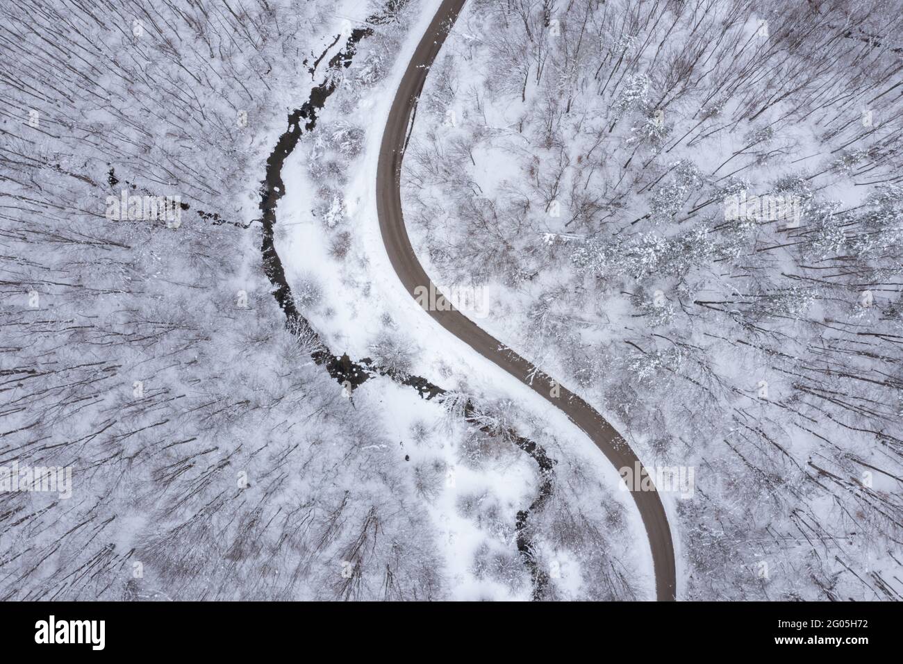 Paysage d'hiver aérien avec route sinueuse et sinueuse parallèle à un ruisseau de montagne sinueux Banque D'Images